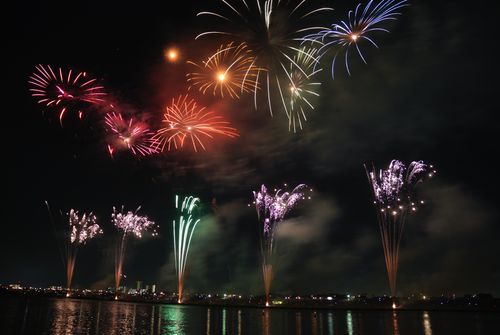 Free Colorful fireworks illuminate the night sky, reflecting beautifully on a river, capturing a festive celebration. Stock Photo