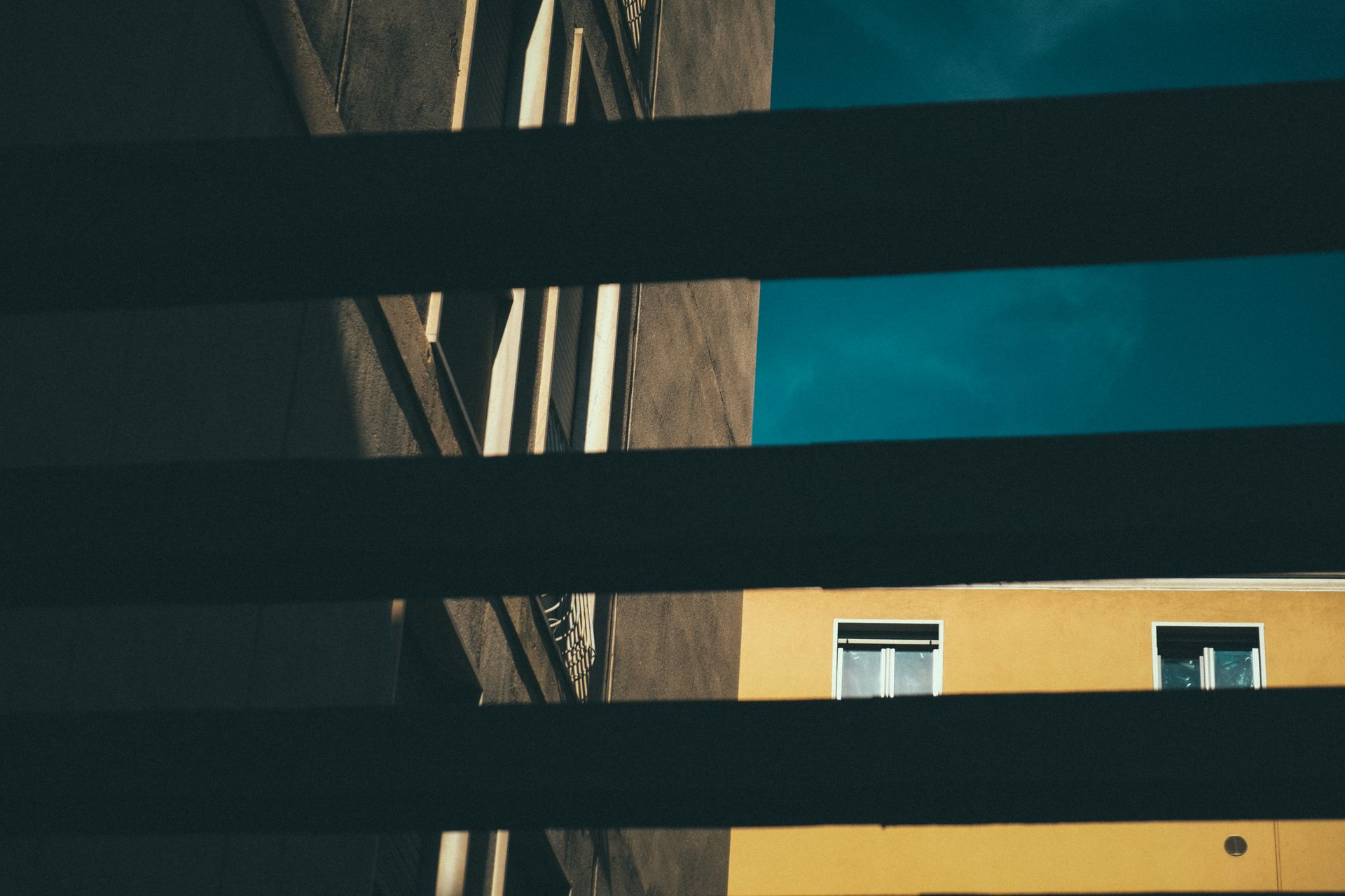 Abstract view of urban architecture with shadows casting across building facades against a blue sky.
