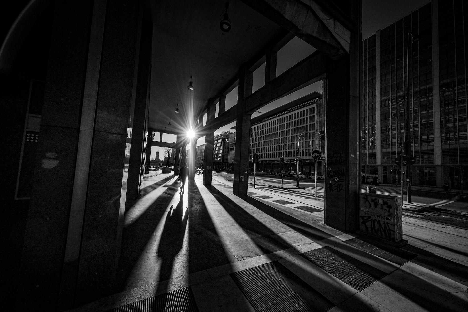 Black and white of anonymous silhouette of person walking along open passage of building