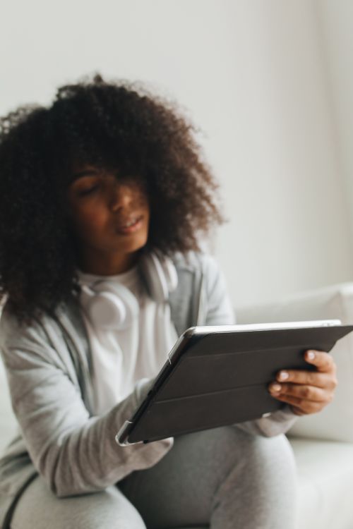 Free African American woman with curly hair using a tablet indoors, focused and engaged. Stock Photo