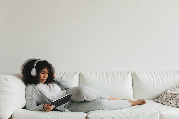 A Woman With A Headphone Lying On A Couch Using A Tablet 