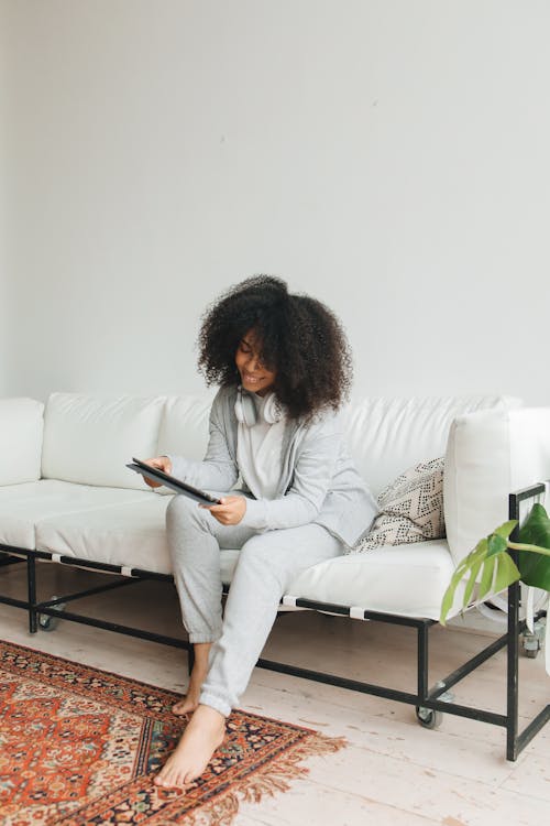 Free An Afro-Haired Woman Using a Tablet while Sitting on a Sofa Stock Photo