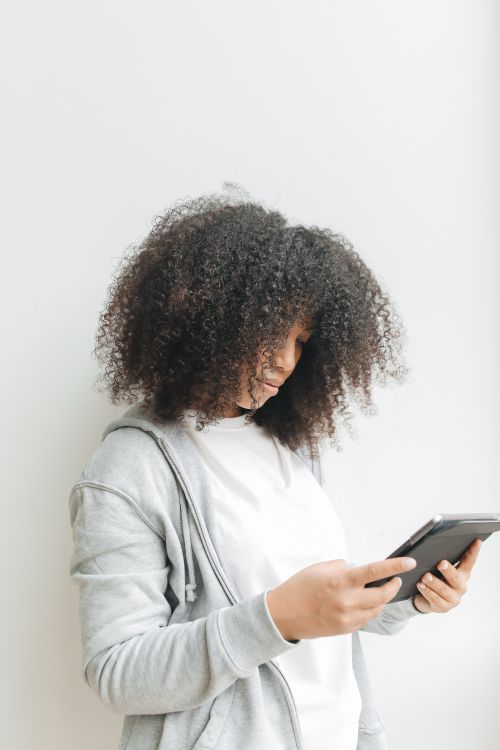 Free Side profile of a young woman with curly hair engaged with a tablet device indoors. Stock Photo