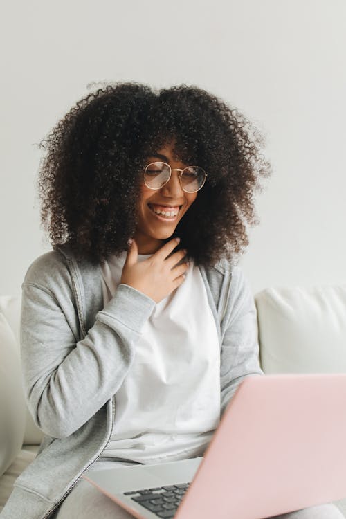 An Afro-Haired Woman in Gray Hoodie Sitting while Using a Laptop