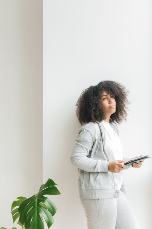Free African American woman casually holding a tablet in a bright, minimalistic space. Stock Photo