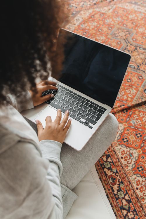 Free Overhead view of a woman with curly hair working on a laptop while seated on a patterned rug indoors. Stock Photo