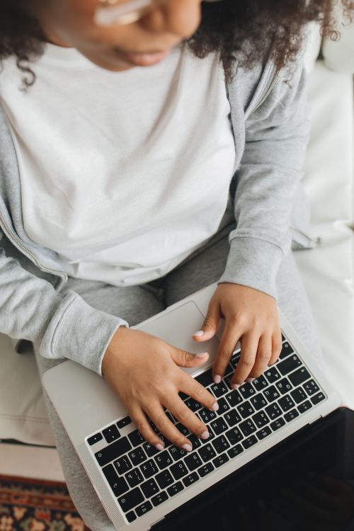 Free A woman with afro hair using a laptop indoors, focusing on modern technology and casual home comfort. Stock Photo