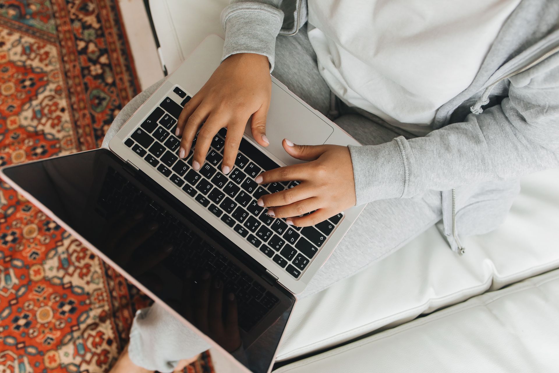 Person working remotely on a laptop from home, sitting on a sofa with a cozy carpet nearby.