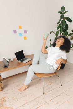 Happy woman enjoying a drink while sitting with gadgets at home.
