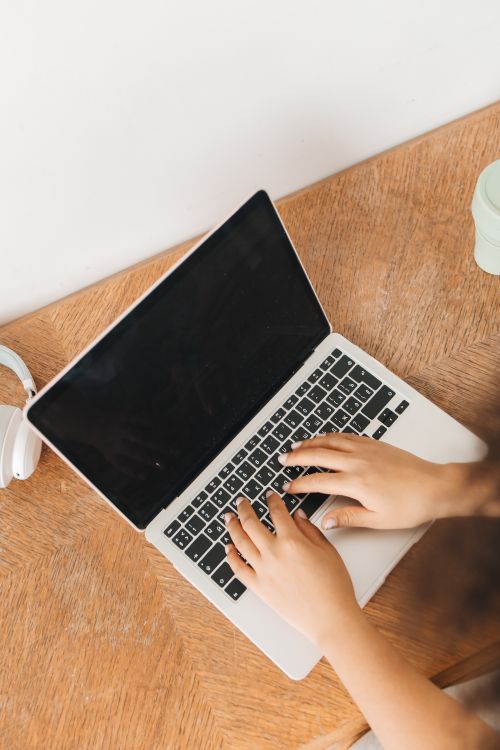 Free Close-up of hands typing on a laptop placed on a wooden table, top view. Stock Photo