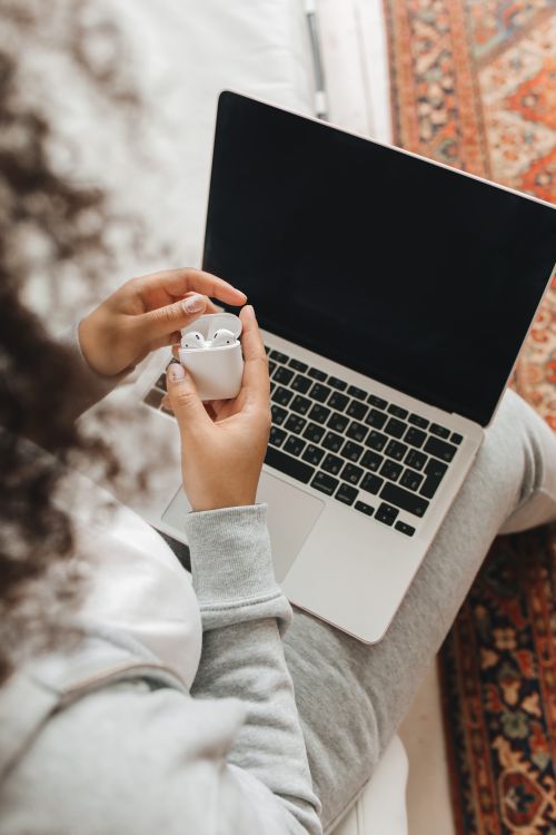 Free Woman holding AirPods near a laptop in a comfortable indoor setting, perfect for tech lifestyle concepts. Stock Photo