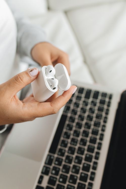 Free Close-up of a woman holding wireless earbuds above a laptop, depicting remote work or study scenario. Stock Photo