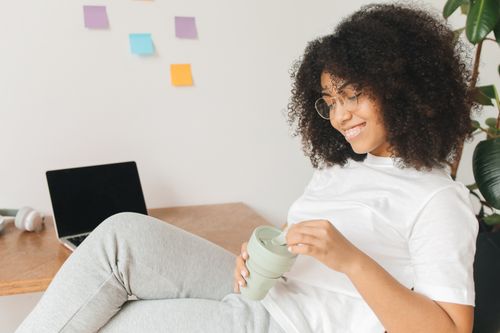 Free Smiling woman sitting comfortably while working remotely with a laptop and coffee. Stock Photo