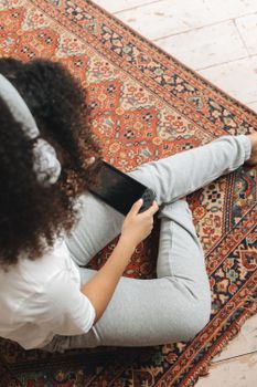 Woman sitting on a patterned rug, playing a Nintendo Switch with white headphones on in a cozy indoor setting.