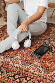 Woman sitting on a carpet holding headphones next to a video game console.