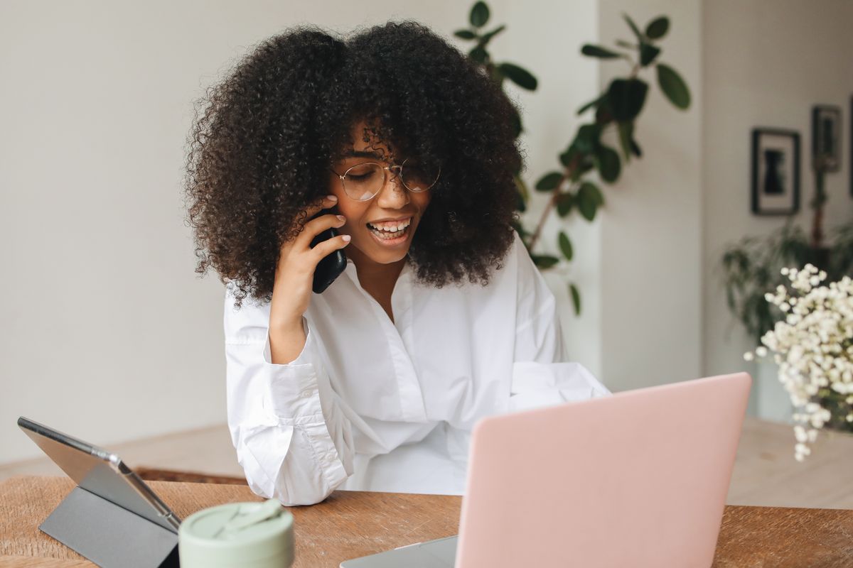 Smiling woman talking on the phone while working on a laptop at home
