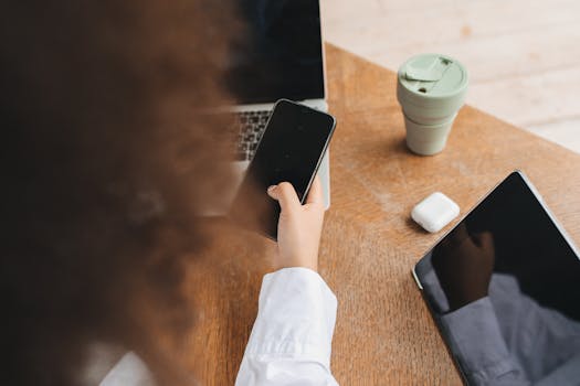 Overhead view of a person multitasking with electronic gadgets and a coffee cup at a home desk.