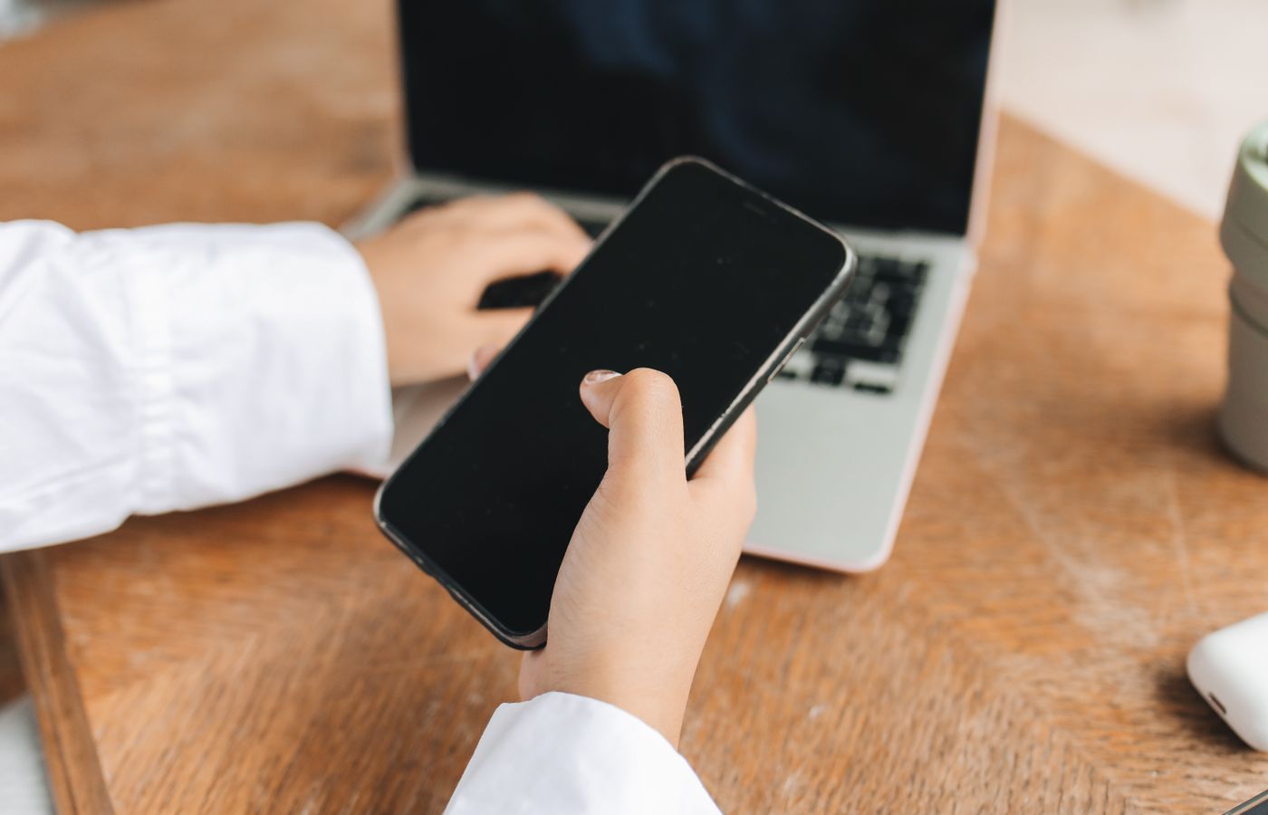 Person using smartphone and laptop in a home office setup, ideal for remote work concepts.