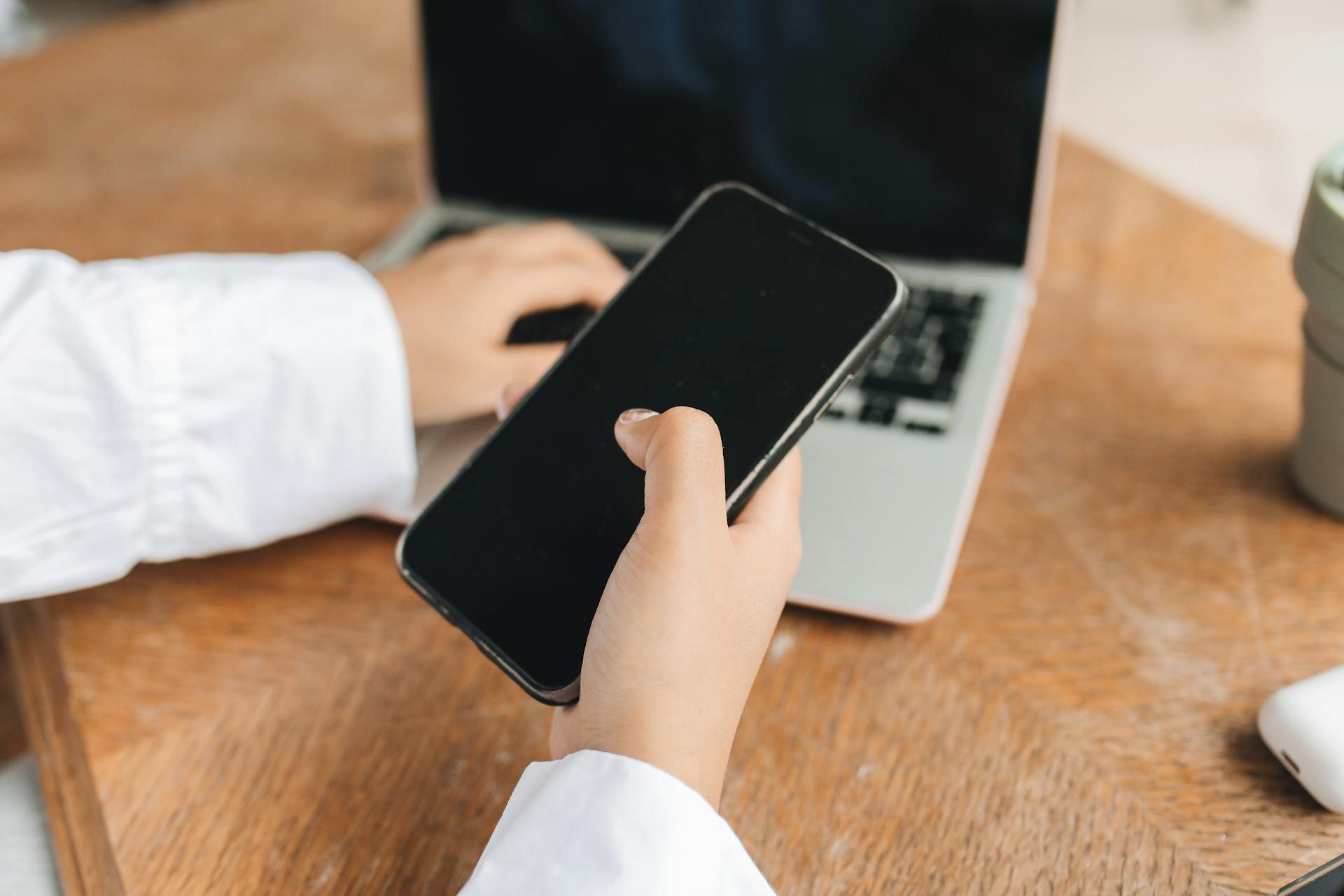 Person using smartphone and laptop in a home office setup, ideal for remote work concepts.