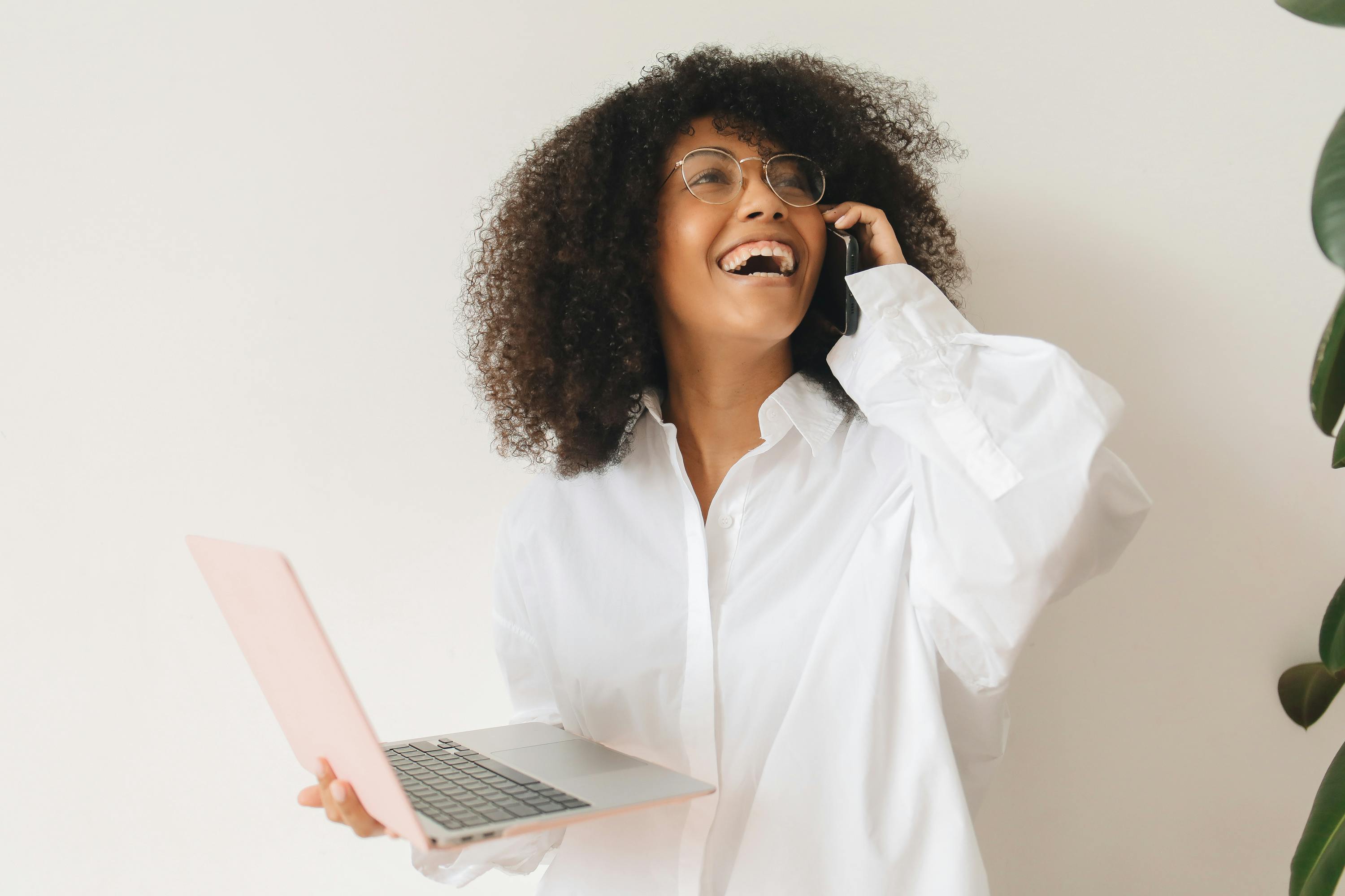 woman in white dress shirt having a phone call while holding a laptop