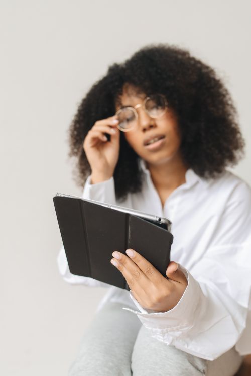 Free Adult woman with afro hair using a tablet indoors with a thoughtful expression. Stock Photo