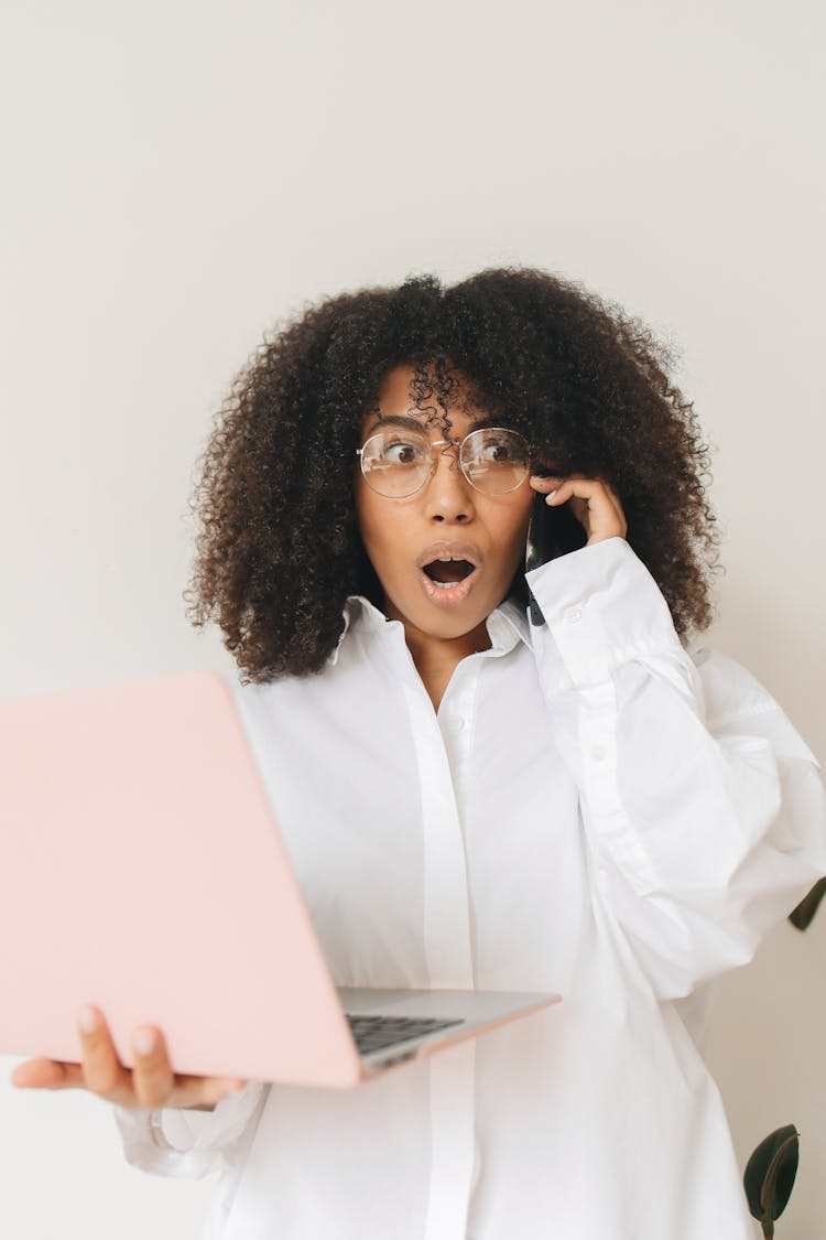 Shocked Woman On Phone Call While Holding A Laptop