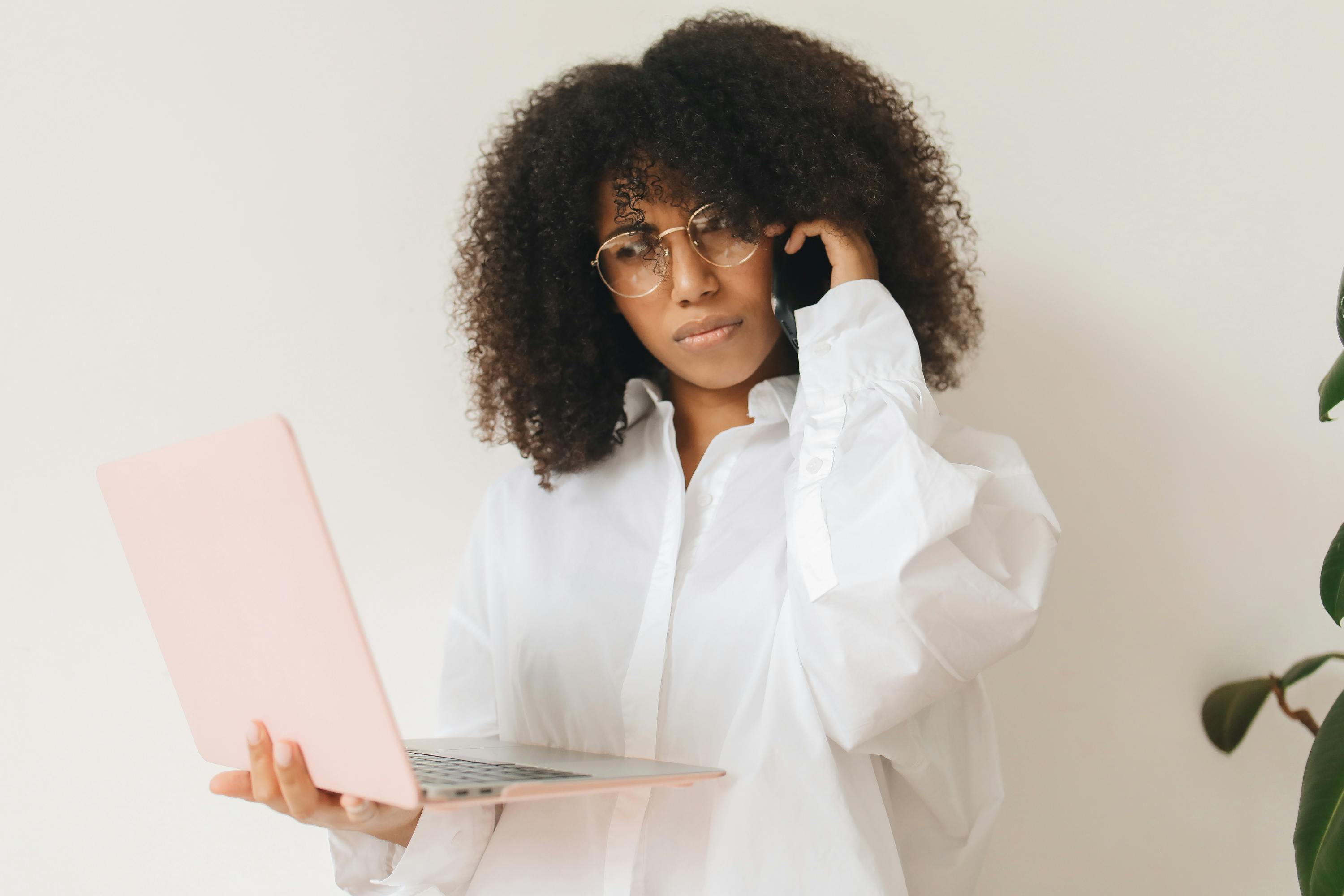 woman in white long sleeve shirt holding laptop while on phone call