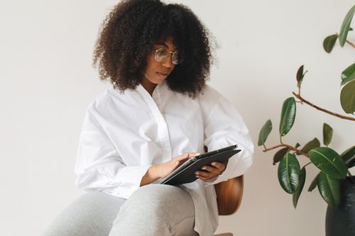 Free Woman in white shirt using a tablet at home, surrounded by indoor plants. Stock Photo