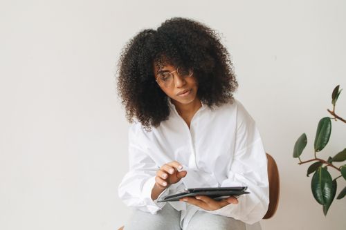 Free A woman with curly hair using a tablet for remote work at home. Stock Photo