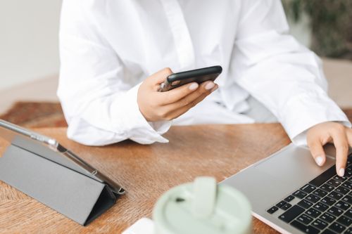 Free Individual in white shirt using a smartphone and laptop indoors. Stock Photo