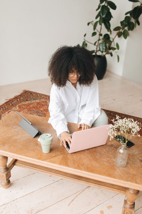 Free Woman working from home with pink laptop, tablet, and indoor plants on a cozy desk. Stock Photo