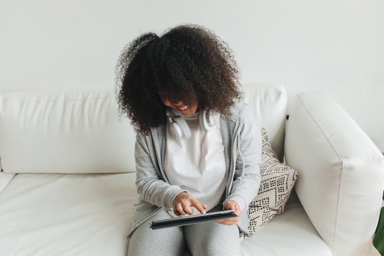 Afro-Haired Woman Sitting On White Couch Using An Ipad