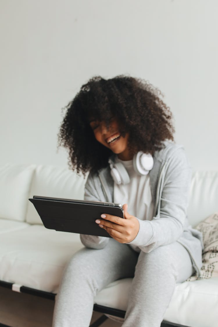 Afro-Haired Woman Sitting On White Couch Using An Ipad