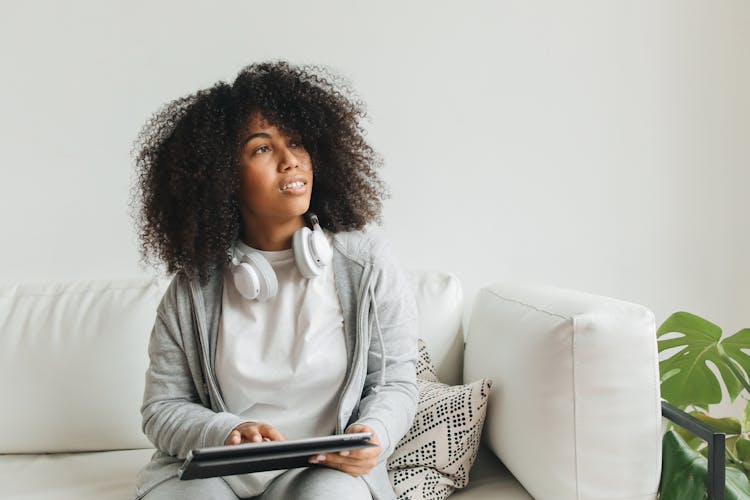 Afro-Haired Woman Sitting On White Couch Using An Ipad