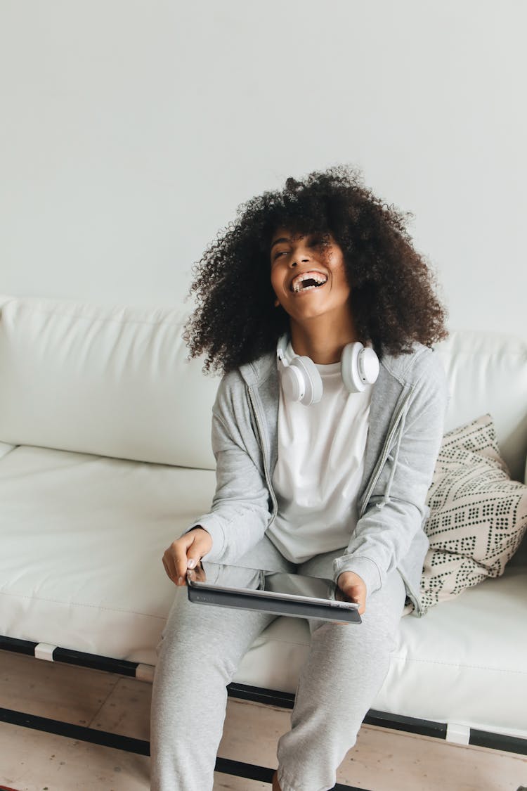 Afro-Haired Woman Sitting On White Couch Holding A Digital Tablet