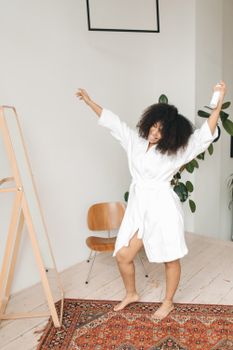 Happy woman in a bathrobe enjoying a moment indoors, holding hairspray.