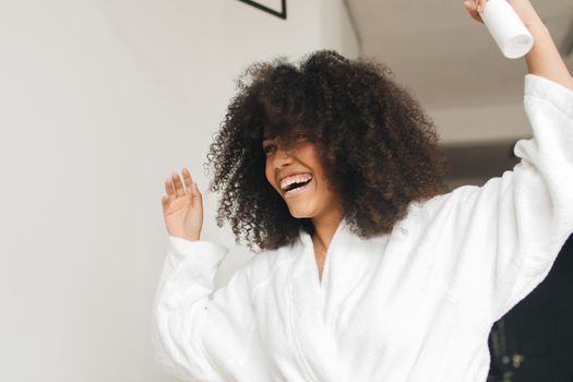 A happy woman with curly hair in a bathrobe, enjoying a carefree moment indoors.