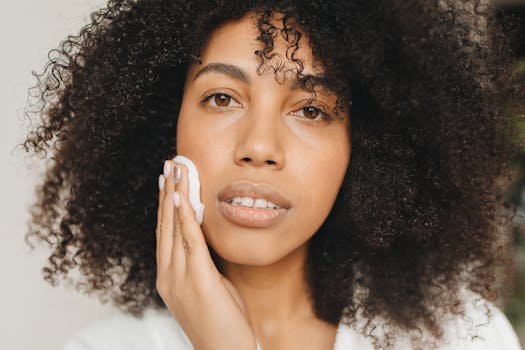 Close-up of a woman with curly hair using a cotton pad for skincare indoors.