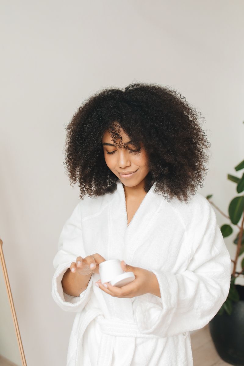 Mujer aplicando mascarilla para método curly en cabello rizado en bata blanca