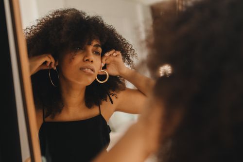 Free A fashionable woman with curly hair adjusts her earrings in the mirror. Stock Photo