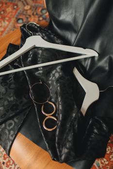 Flat lay of a black dress, gold earrings, and hangers on a patterned rug.