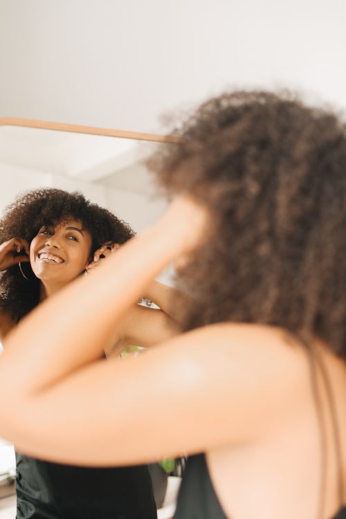 Free Happy woman adjusting earrings and smiling in front of a mirror at home. Stock Photo