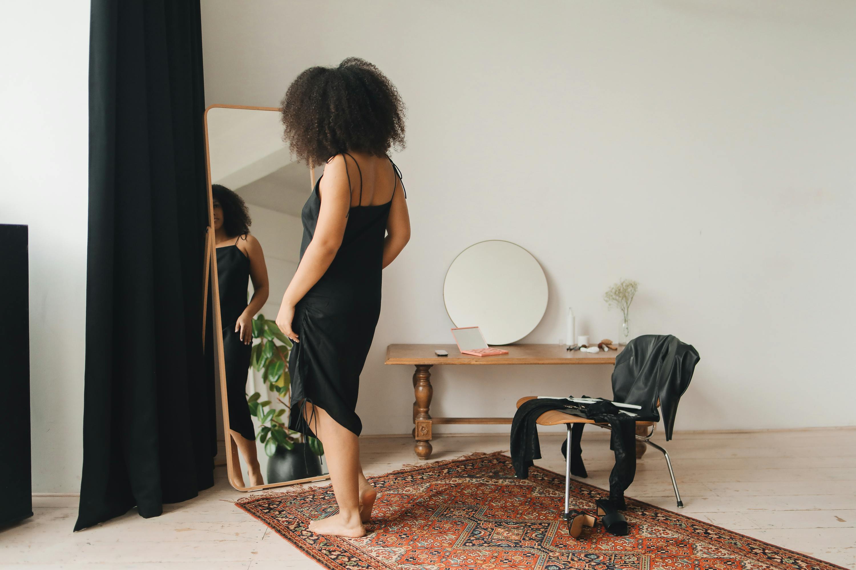 Black woman in elegant dress getting ready in front of a mirror in a cozy home setting.