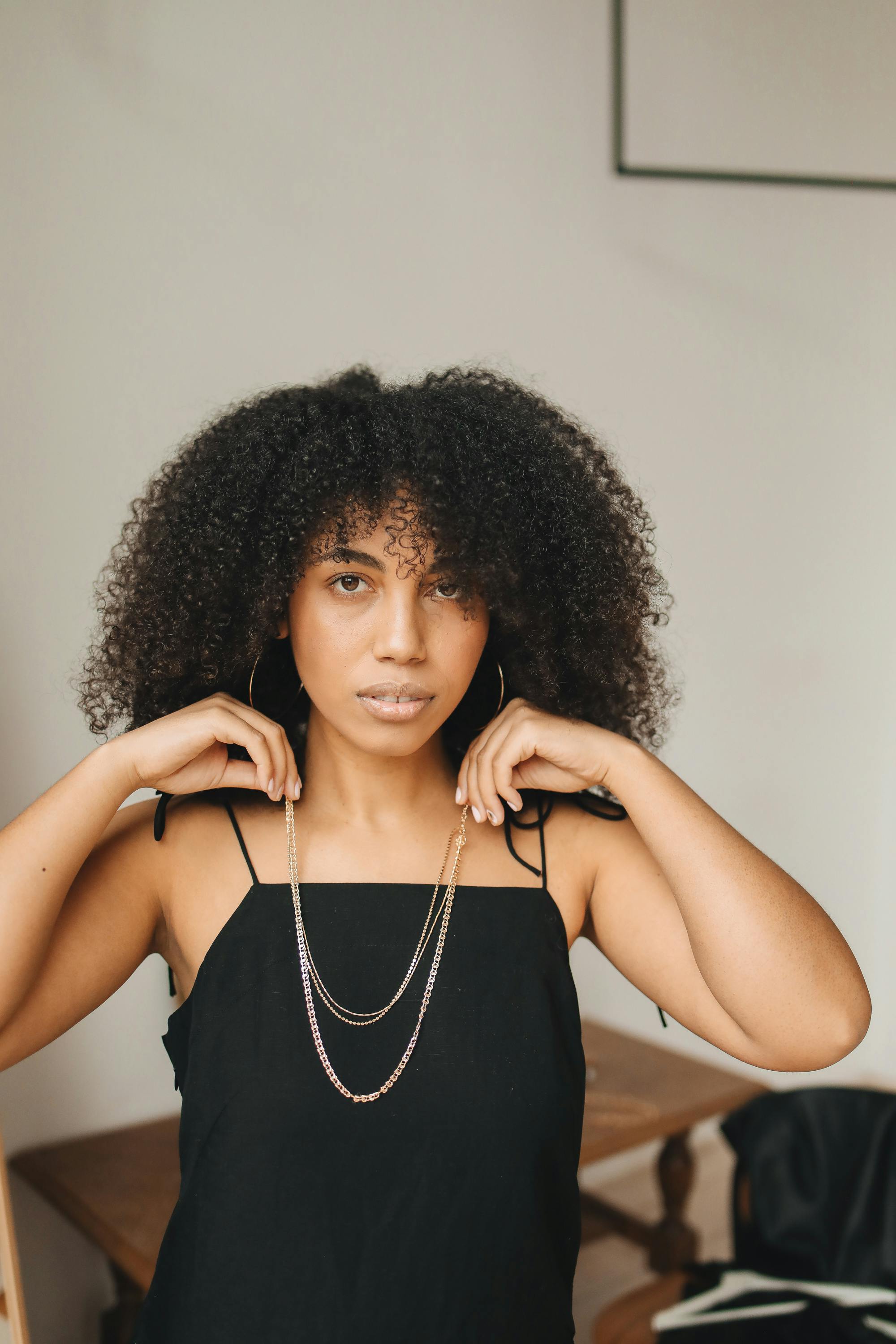 A fashionable woman adjusting her necklace indoors with a casual yet glamorous vibe.