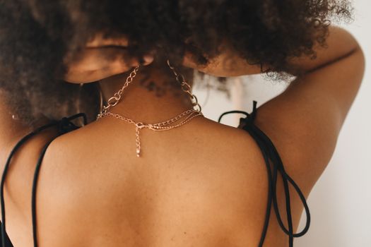A woman elegantly adjusting her necklace at home, highlighting fashion detail.
