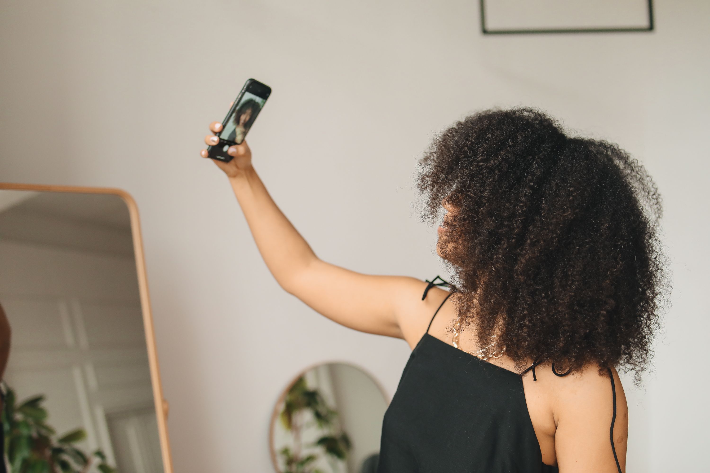 Woman with curly hair taking a monthly progress photo in a mirror at home