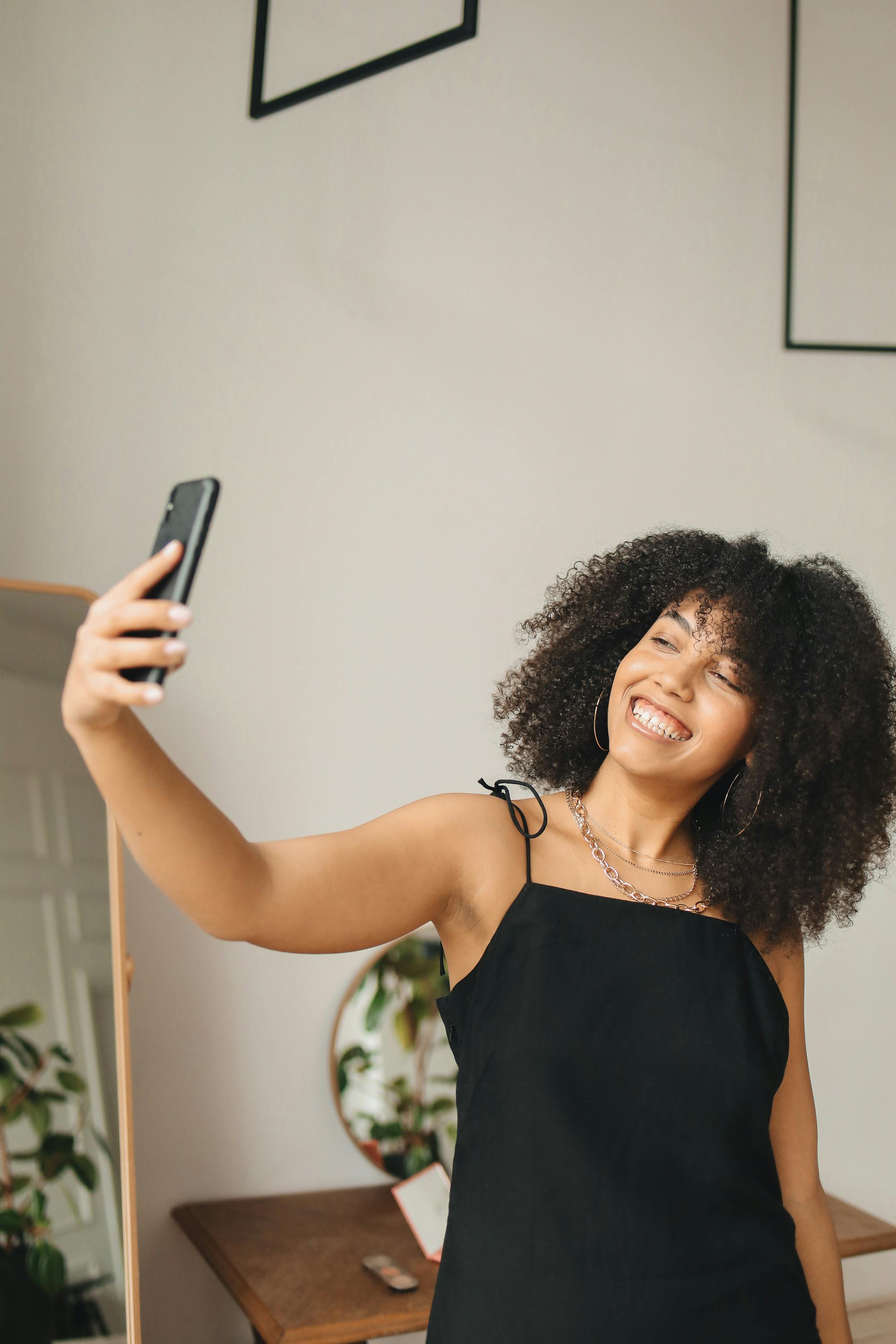 身着黑色连衣裙的微笑女子在室内自拍，展示时尚和生活方式