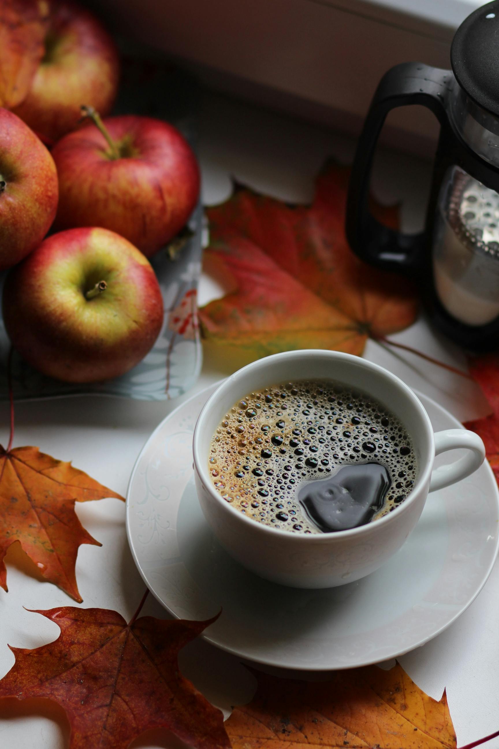 Warm coffee with apples and autumn leaves, creating a cozy fall atmosphere.