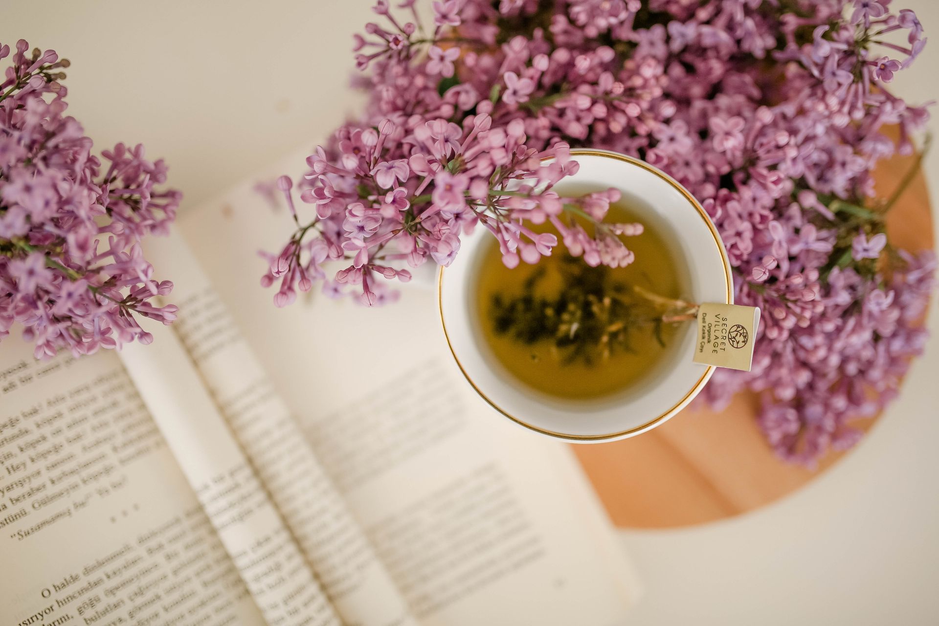 A calming setup with a teacup of herbal tea surrounded by lilac blooms and an open book.