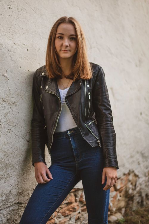 Free Stylish woman in a leather jacket leaning against a wall, outdoors. Stock Photo
